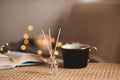 Home liquid fragrance in glass bottle with cup of coffee and paper book on rattan table over xmas lights close up. Royalty Free Stock Photo