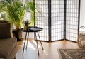 Home living room with wood and paper divider screen blocking sun from window, black metal accent table and sofa.