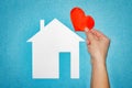 Home love concept. female hand with red heart over white paper house on blue background Royalty Free Stock Photo