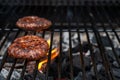 Home-made juicy beef burgers grilled on the barbecue. Fire from the charcoal beneath the hamburger.