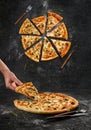 Home made original italian pizza with human hand holding pizza slice. Top view separated pizza slices on black grunge Royalty Free Stock Photo