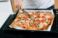 Home made pizza. Person cutting cooked fresh pizza with cheese, tomato, mozzarella, chicken and mushrooms on modern white kitchen Royalty Free Stock Photo