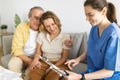 Home nurse on visit to senior couple at home, sitting on couch and talking, discussing results of medical exams Royalty Free Stock Photo