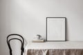 Home office concept. Empty black vertical picture frame mockup. Cup of coffee on old books, linen table cloth. White