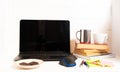 Home office concept. Work from home. Black laptop, books and cafe cuo on the white wooden background. Side view. Sweden.