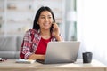 Home Office Concept. Young Asian Female Talking On Cellphone And Using Laptop Royalty Free Stock Photo