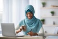 Home Office. Black muslim freelancer lady drinking coffee and writing in notepad Royalty Free Stock Photo