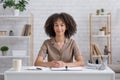 Cute african american girl with notebook and headphones sits at table and looks at camera