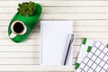 Home office workspace mockup with notebook, pen, cup of coffee,  plant potted on green tray and accessories on white wood desk Royalty Free Stock Photo