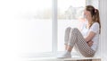 Home quarantine banner. A Caucasian woman on sick leave is sitting at the window in a medical protective mask, looking sadly at Royalty Free Stock Photo