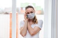 Home quarantine. Caucasian woman on sick leave in a medical protective mask, calls the phone, calls an ambulance. Poor health, Royalty Free Stock Photo