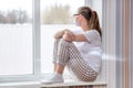 Home quarantine. Caucasian woman on sick leave is sitting at window in a medical protective mask, looking sadly at street. Poor Royalty Free Stock Photo