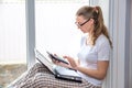 Home quarantine. Remote work at home. Caucasian woman sitting at window with a computer.Counts on calculator and writes in a Royalty Free Stock Photo