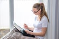 Home quarantine. Remote work at home. Caucasian woman sitting at window with a computer.Counts on calculator and writes in a Royalty Free Stock Photo