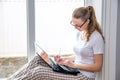 Home quarantine. Remote work at home. Caucasian woman sitting at window with a computer.Counts on calculator and writes Royalty Free Stock Photo