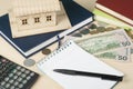 Home savings, budget concept. Model house, notepad, pen, calculator and coins on wooden office desk table. Royalty Free Stock Photo