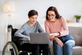 Home schooling concept. Disabled teen boy in wheelchair studying new online materials together with his mother indoors