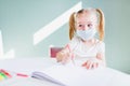 Home schooling learning during virus pandemic. Little girl drawing at home, wearing surgical face masks to protect from the virus