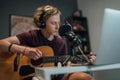 Home sound studio young teenager portrait playing guitar in Headphones with the microphone on the foreground. Modern audio