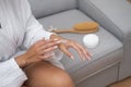 close-up reveals a woman, bathrobe-clad, applying moisturizing cream to her hand, body skincare