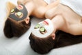 Home spa. Two women holding pieces of cucumber on their faces lying the bed. Royalty Free Stock Photo