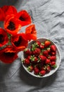 Home still life - ripe fresh strawberries in a bowl and a bouquet of red poppies on a gray background, top view Royalty Free Stock Photo