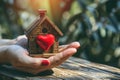 Home sweet home concept. Dream housing. Real estate. Hands holding miniature house with a red heart outdoors on a sunny summer day Royalty Free Stock Photo