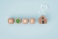 HOME text with smiling face instead of O on wooden cube block and miniature wood house with blurred white heart above , for warm Royalty Free Stock Photo