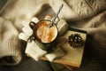 At home, there is a stack of old books, on which are wool gloves, a fir cone and a mug of cappuccino, which is sprinkled with