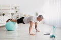 Home training. Athletic mature man planking with fitball in front of laptop, having online fitness class from home