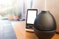 Home weather station with white screen and black humidifier fuming water steam near the window on a sunny day