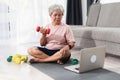 Home workout concept, Asian elderly woman doing exercise, lifting dumbbells, looking at laptop