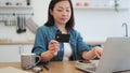 Homebody behind laptop looking at bank card in kitchen