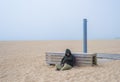 Homeless adult man person with hood sitting and sleeping on sandy beach Royalty Free Stock Photo