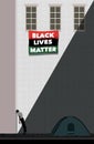 A homeless African American man leans in despair against a wall in an urban alley. A Black Lives Matter banner waves from windows Royalty Free Stock Photo