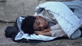 Homeless african teenager lying in sleeping bag ground, poverty unemployment Royalty Free Stock Photo