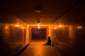 Homeless beggar on his knees begs for alms in a dark underpass.