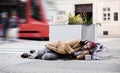 Homeless beggar man lying on the ground outdoors in city asking for money donation. Royalty Free Stock Photo
