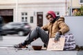 Homeless beggar man sitting outdoors in city asking for money donation.