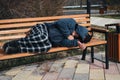 homeless dirty elderly old Caucasian man lies sleeping on park bench in autumn Royalty Free Stock Photo