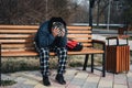 homeless elderly old Caucasian man with depression holds head in hands while sitting on park bench