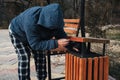 homeless elderly old Caucasian man rummages for food and garbage in trash can in a park in autumn