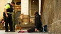 PRAGUE, CZECH REPUBLIC, SEPTEMBER 9, 2019: Homeless girl begging tourists throw coin money into cap, a police officer