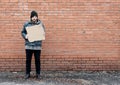 Homeless holds piece of cardboard. Refugee is at brick wall looking for job. Male tramp in dirty clothes. Below poverty line. Royalty Free Stock Photo