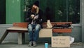 Homeless and jobless european man with cardboard sign eat sandwich on bench at city street because of immigrants crisis Royalty Free Stock Photo