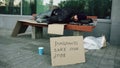 Homeless and jobless european man with cardboard sign sleep on bench at city street because of immigrants crisis in Royalty Free Stock Photo