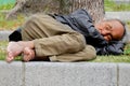 Homeless male sleeping under a tree barefoot