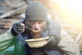 A homeless man eats soup from a plate near the ruins, helping poor and hungry people during the epidemic, sun glare on the image