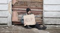 Homeless man sits and holds piece of cardboard with inscription Help. Refugee looking for job. Male tramp in dirty clothes, hat