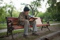 Homeless man sitting on bench holding book in hands. Royalty Free Stock Photo